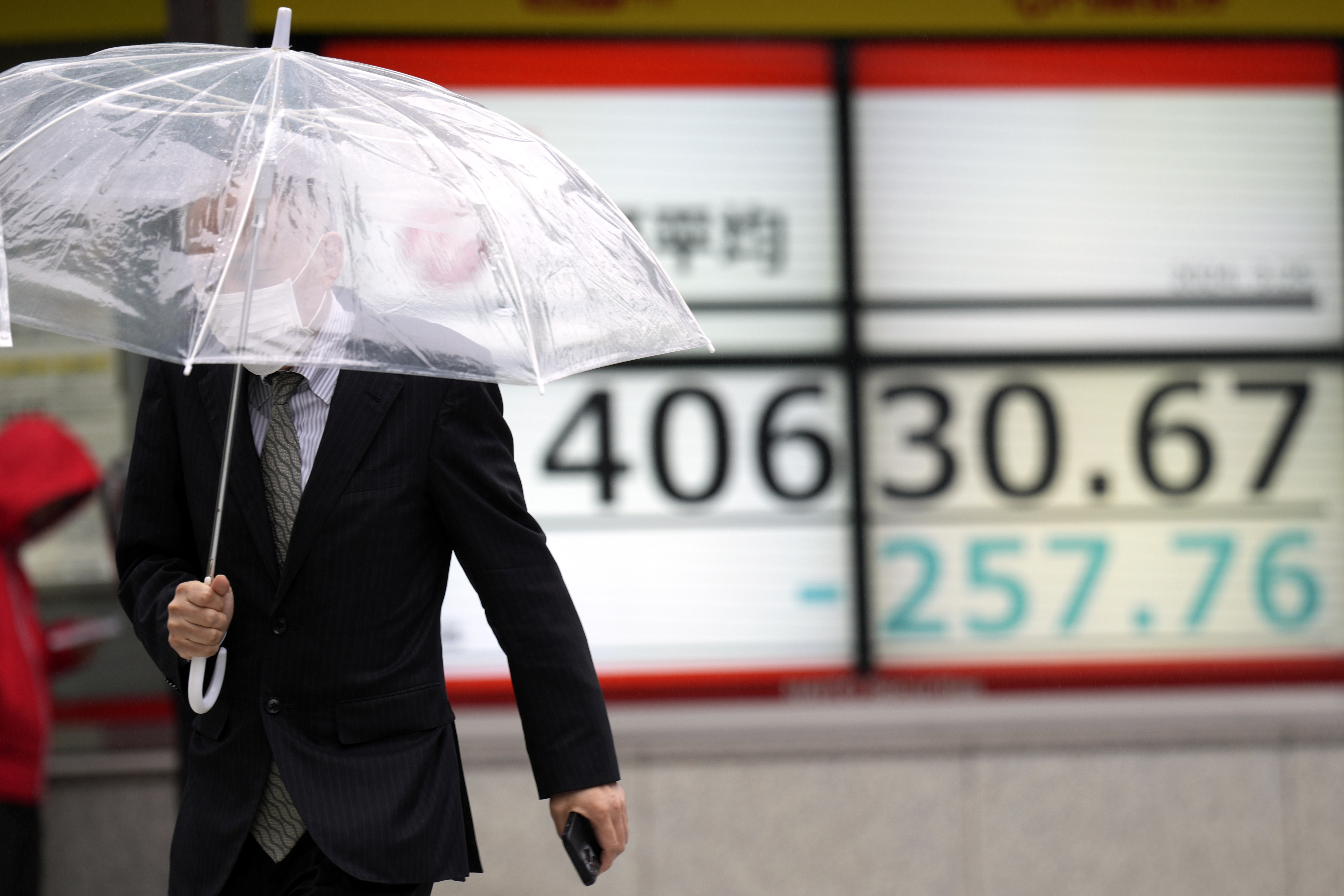A person walks in front of an electronic stock board showing Japan's Nikkei 225 index at a securities firm in the rain Monday, March 25, 2024, in Tokyo. Asian shares were trading mixed on Monday, as investors awaited further indications the Federal Reserve might begin cutting interest rates.(AP Photo/Eugene Hoshiko)