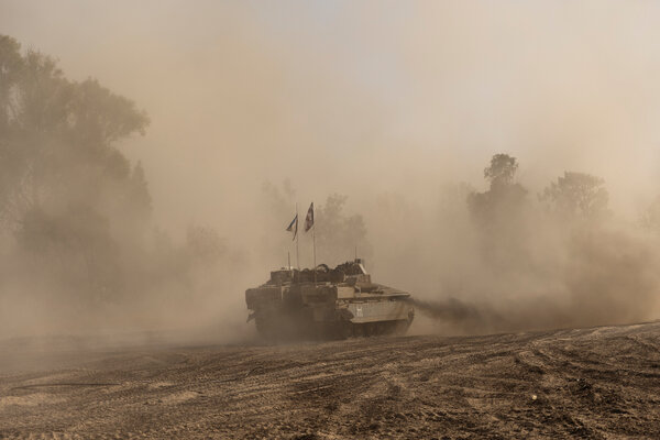 A tank driving through the sand, with trees in the background. 