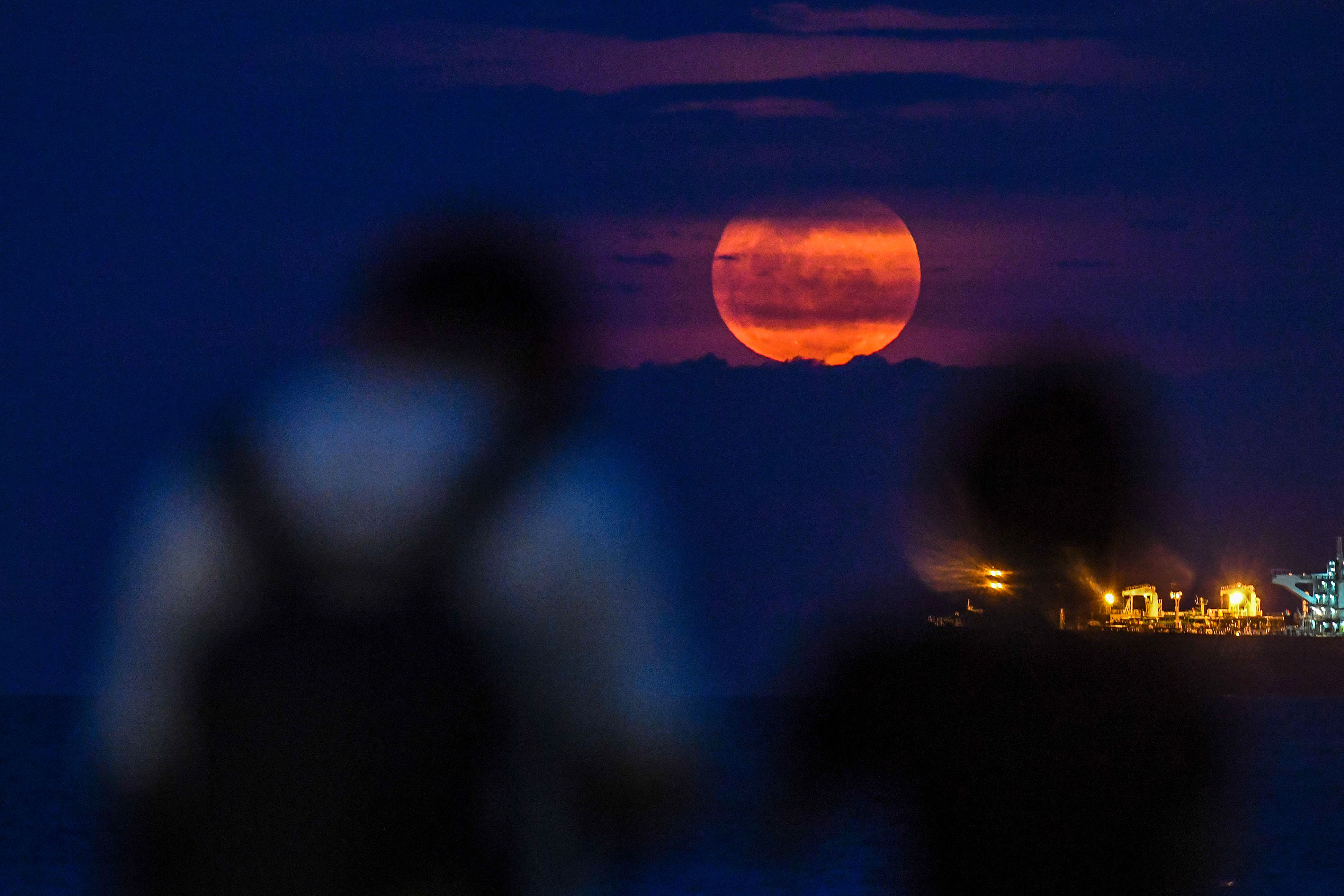 TOPSHOT - People watch the April's full moonset, also known as the
