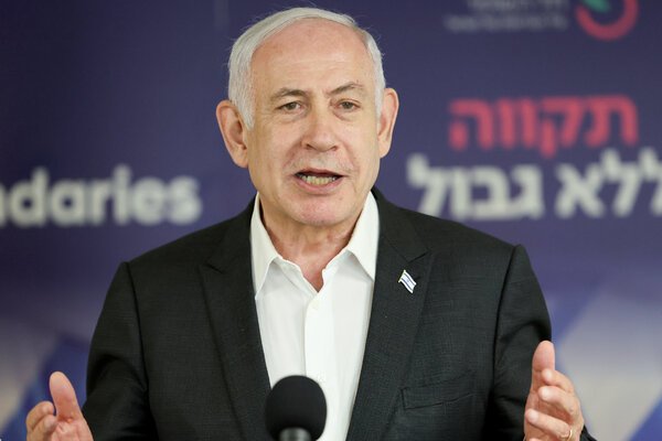 Benjamin Netanyahu stands behind a microphone wearing a dark suit with a lapel pin of the Israeli flag.