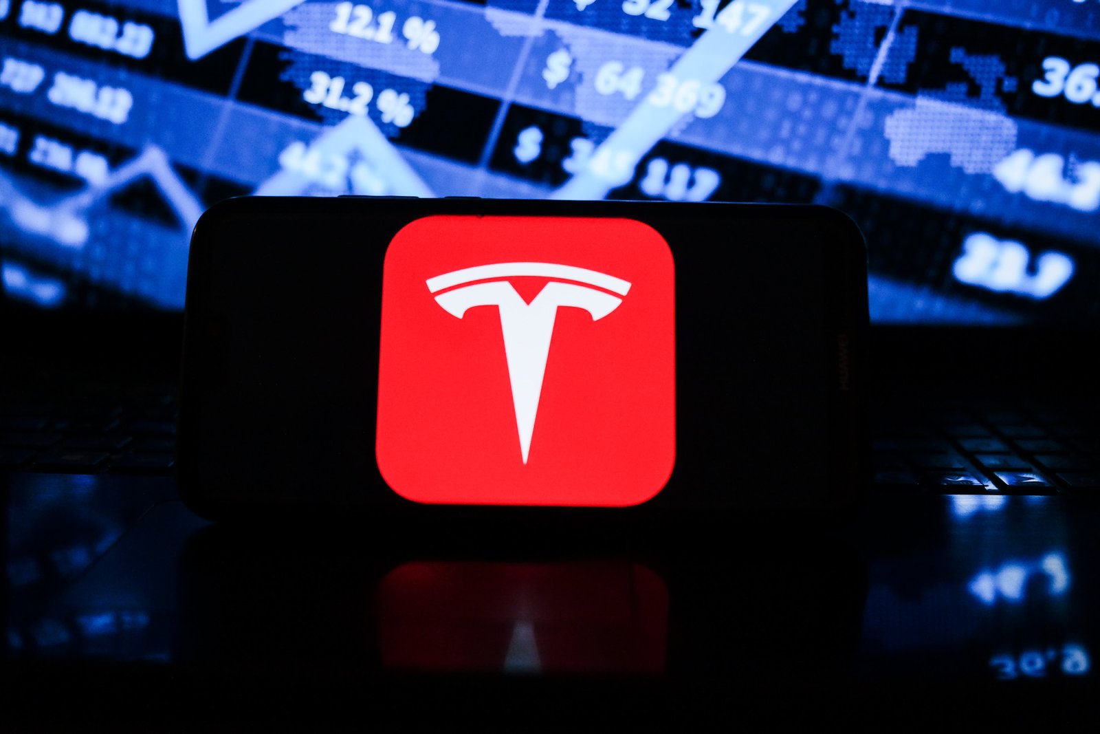 In this photo illustration a Tesla logo seen displayed on a smartphone with the stock market graphic in the background.