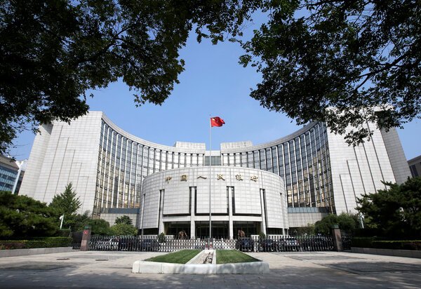 The white, semicircle shaped exterior of the People’s Bank of China building, with a Chinese flag in front. 