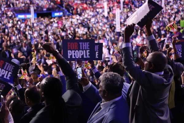 A large crowd in a convention center, with some people holding signs saying, 