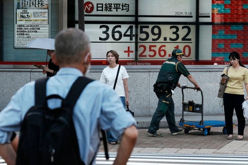 People stand near an electronic stock board showing Japan's Nikkei index at a securities firm Wednesday, Sept. 18, 2024, in Tokyo. (AP Photo/Eugene Hoshiko)