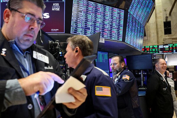 Traders on the floor of the New York Stock Exchange. Behind them are screens with stock prices.