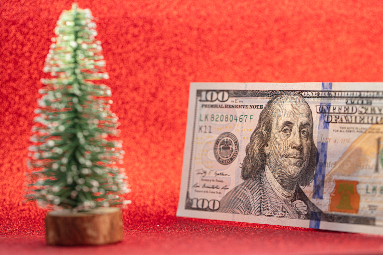 100 dollar bill and toy fir tree on red background for design purpose