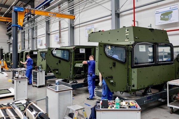 Workers in blue uniforms are working on cabins for military trucks at a plant.