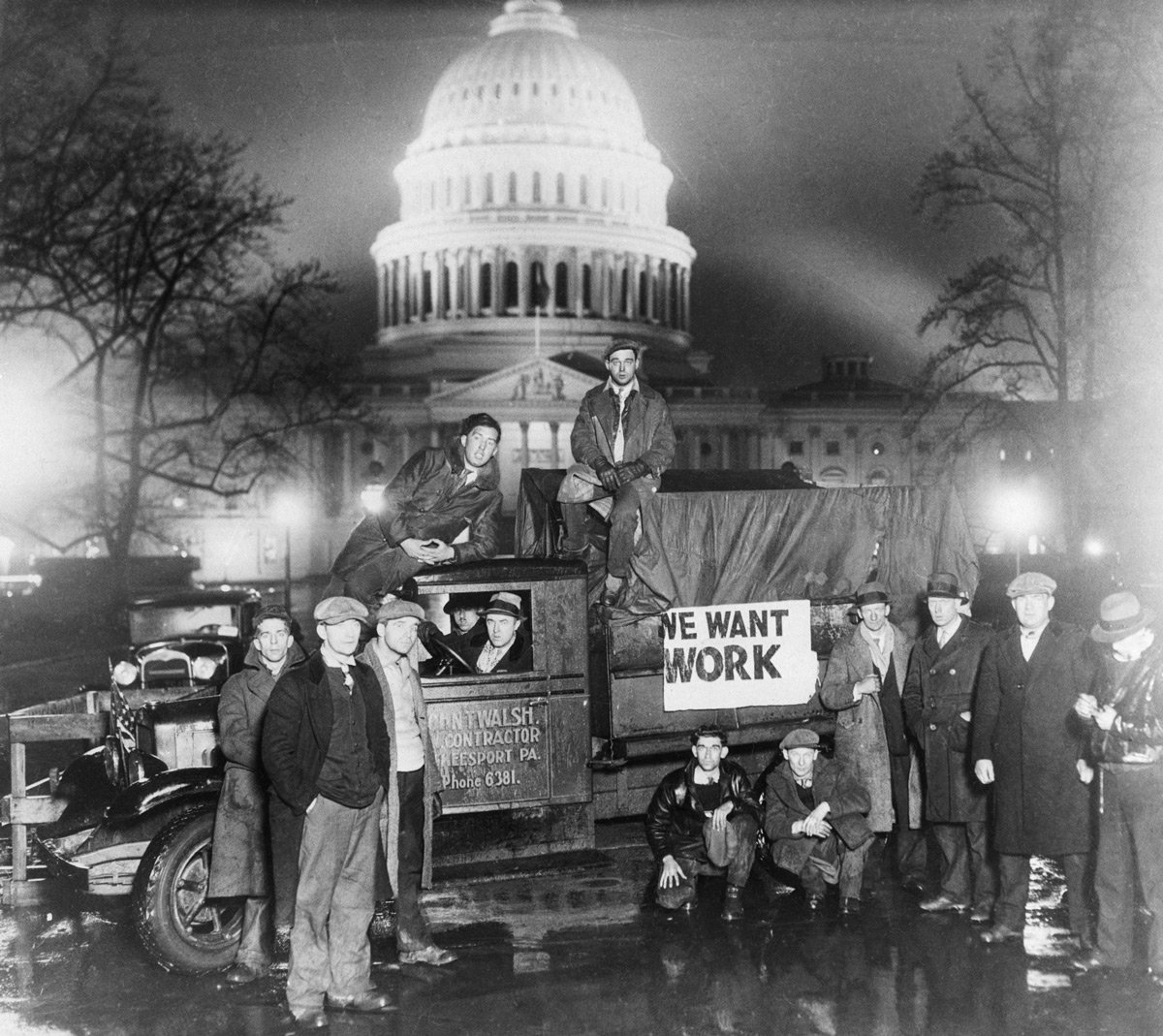 A group of men, several seated on and around a truck with a sign reading 