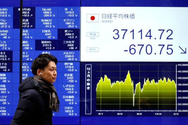 A man walks past a large screen showing that the Nikkei stock index fell sharply on Tuesday. 