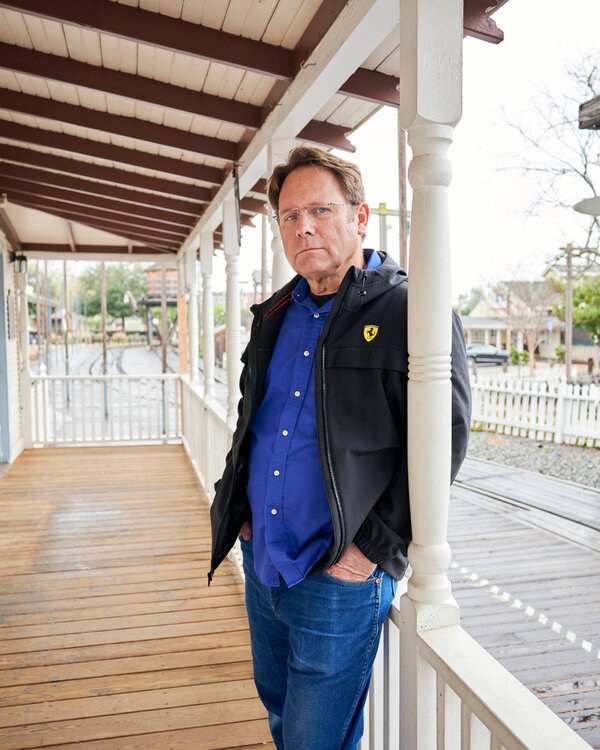 Lars Staack stands against a white porch pillar wearing jeans, a blue shirt and a dark jacket.