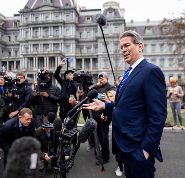 Treasury Secretary Scott Bessent gestures with his right hand while speaking outside next to a group of cameras and microphones. The Eisenhower Executive Office Building is in the background.