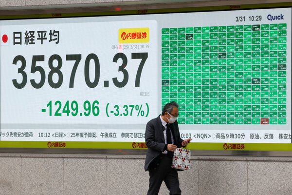 A person walks past a giant video screen showing stock market data.