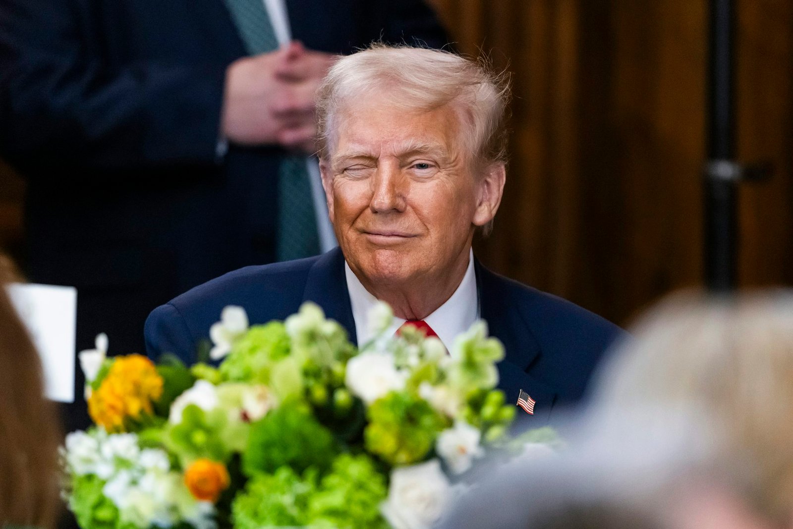 Trump winks as he sits at a table.