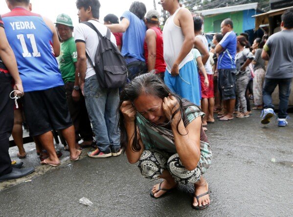 FILE- An unidentified relative cries as people look at the body of a woman, later identified by her husband as that of Nora Acielo, after she was shot by still unidentified men while about to bring her two children to school at a poor neighborhood in Manila, Philippines Thursday, Dec. 8, 2016. Police said the killing of Acielo was the 13th recorded drug-related case in the past 24 hours in President Rodrigo Duterte's unrelenting war on drugs. (AP Photo/Bullit Marquez, File)