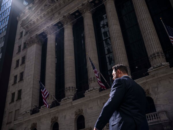 A man in a blue suit walks in front of a stone building with pillars.