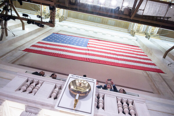 A photograph of the bell of the New York Stock Exchange taken from below, with a large American flag above it.
