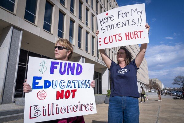 High School teacher June Kelly, left, and SJ Marcotte, right, who teaches business leadership, both with a group of educators from Vermont, hold signs in support of the Department of Education, Thursday, March 20, 2025, outside the department in Washington. (AP Photo/Jacquelyn Martin)