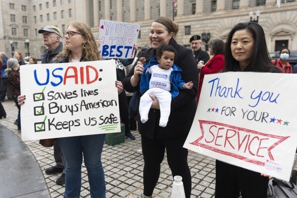FILE - United States Agency for International Development (USAID) supporters hold banners as USAID workers retrieve their personal belongings from the USAID's headquarters in Washington, Feb. 27, 2025. (AP Photo/Manuel Balce Ceneta, File)
