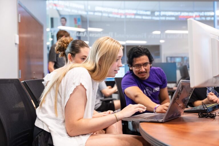One female and one male student look at a computer screen in a classroom. 