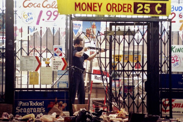 In this April 30, 1992 file photo, a Los Angeles police officer takes aim at a looter in a market at Alvarado and Beverly Boulevard in Los Angeles during the second night of rioting in the city. (AP Photo/John Gaps III, file)