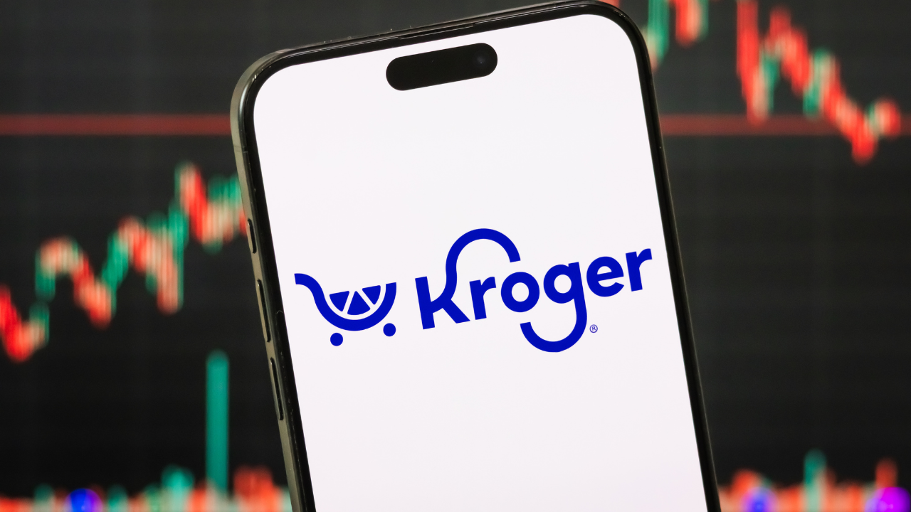 The logo of Kroger Co. displayed on a smartphone screen, with the company's latest stock market chart in the background
