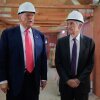 This photo shows President Trump and Federal Reserve Chair Jerome Powell standing next to one another in a large room that's undergoing renovations, with wooden ceiling beams exposed and plywood walls. Both men are wearing white hard hats and suits.