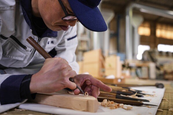 A craftsman uses a chisel while making a Shinto shrine alter at Miyachu factory, which also crafts miniature replicas of the Ise Jingu shrine, in Tamaki, central Japan, Thursday, May 1, 2025. (AP Photo/Hiro Komae)