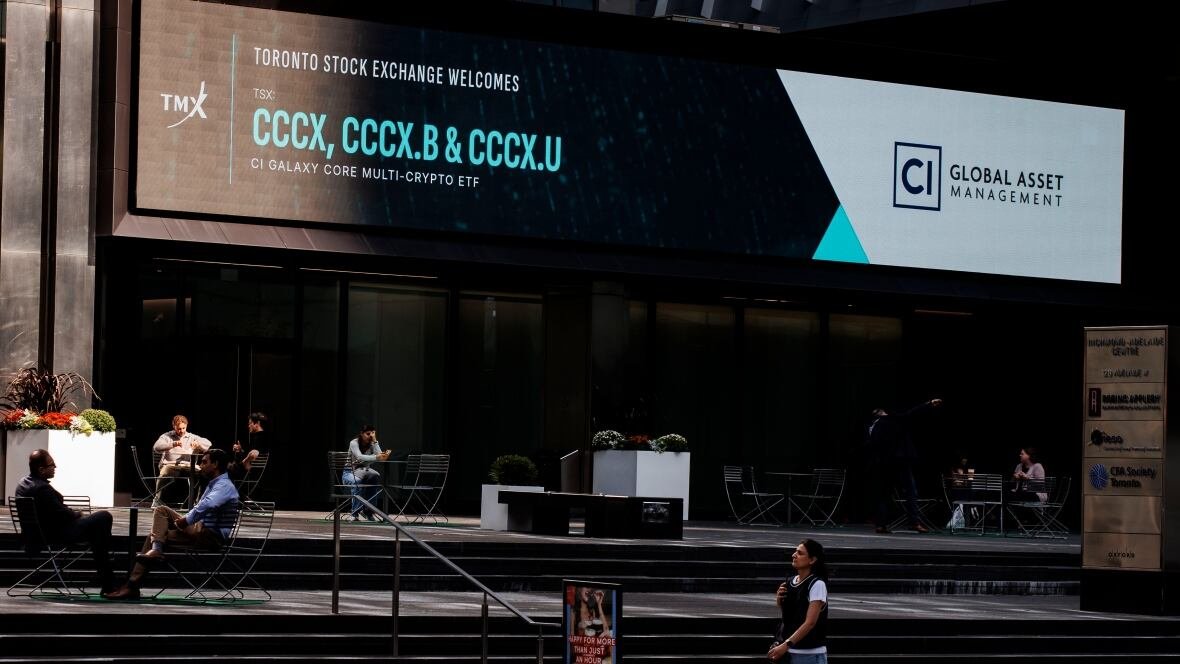 people sit outside the toronto stock exchange building and a woman walks by on the sidewalk