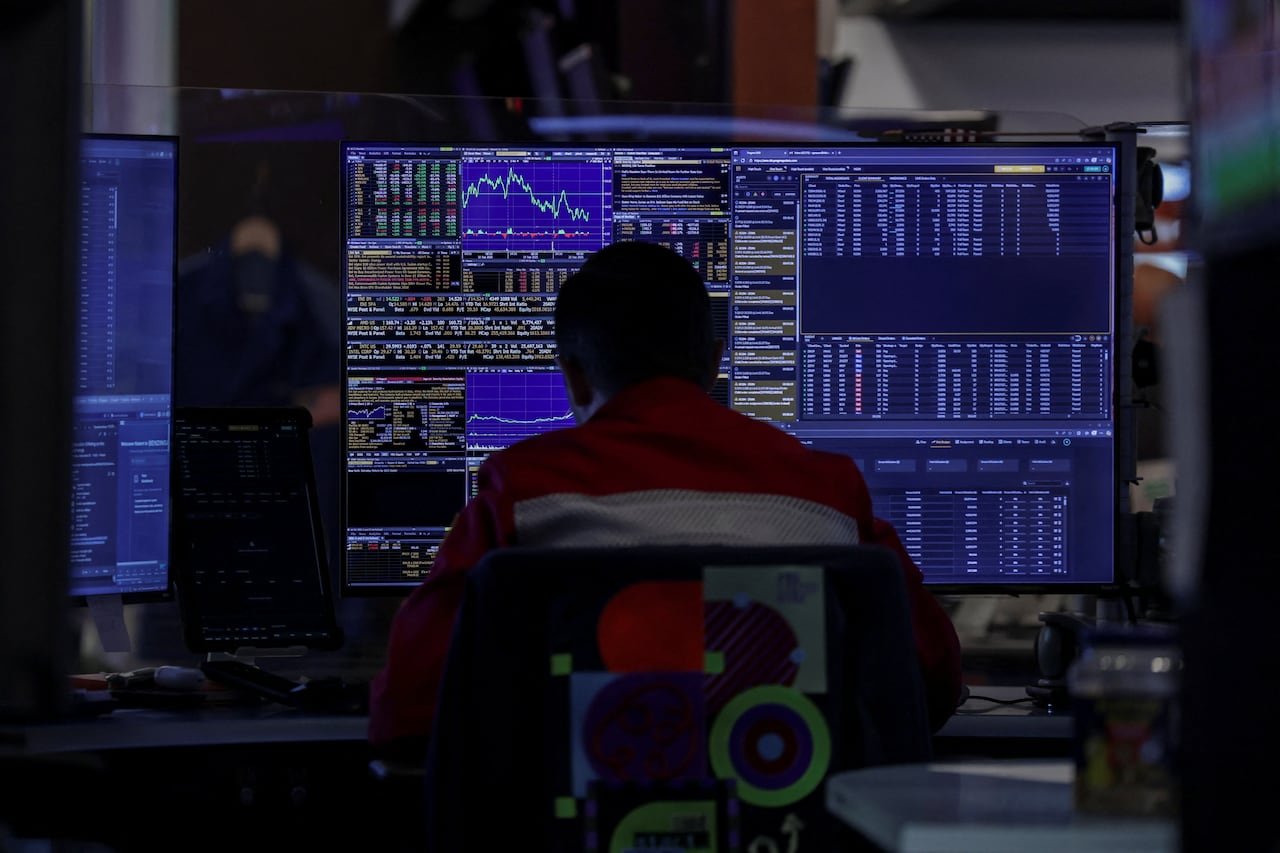 A trader is seated at a computer showing stock market graphics.