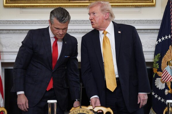 FILE: President Donald Trump talks with Defense Secretary Pete Hegseth after a roundtable on criminal cartels in the State Dining Room of the White House, Thursday, Oct. 23, 2025, in Washington. (AP Photo/Evan Vucci), File