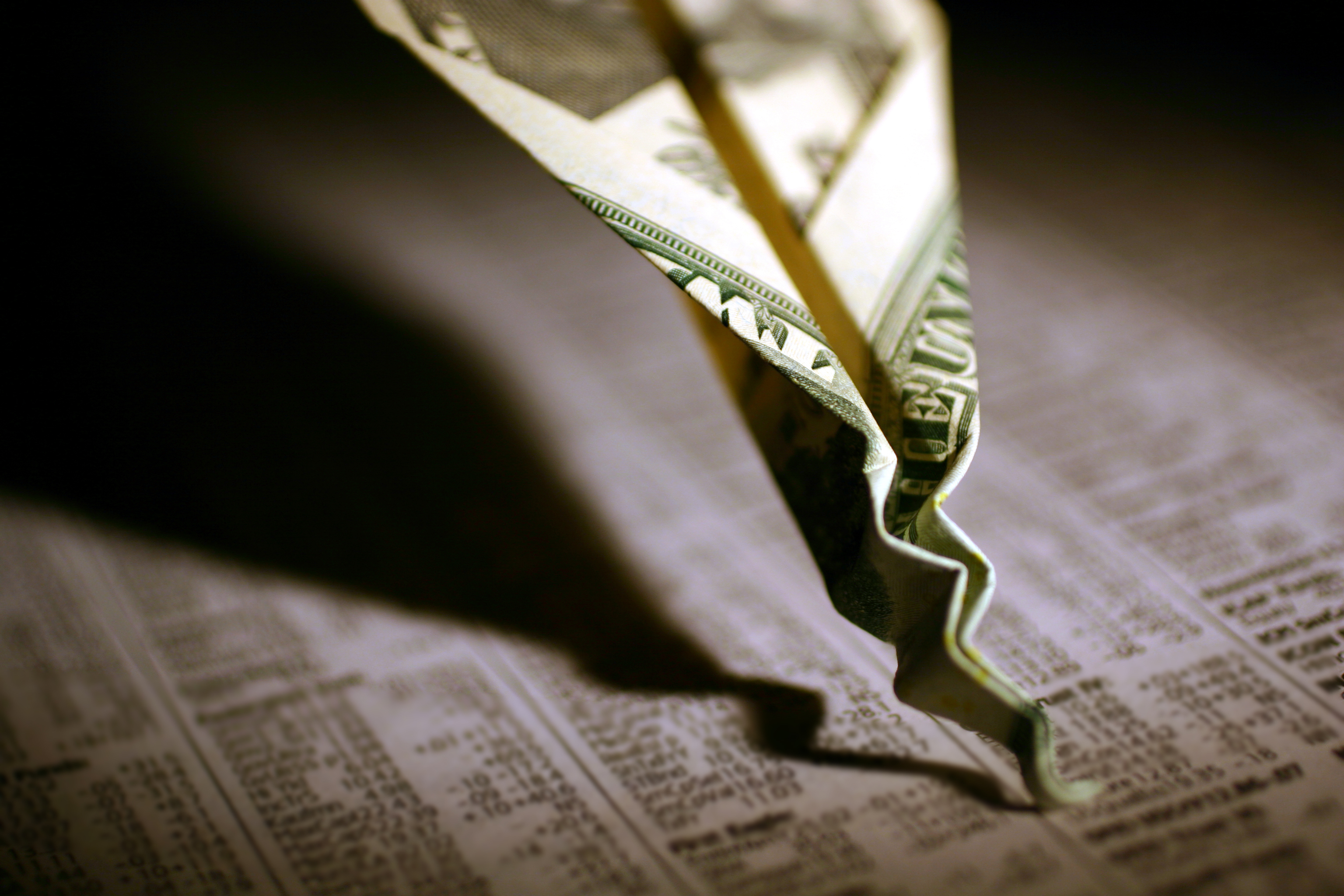 A twenty-dollar bill paper airplane that's crashed and crumpled into a financial newspaper.