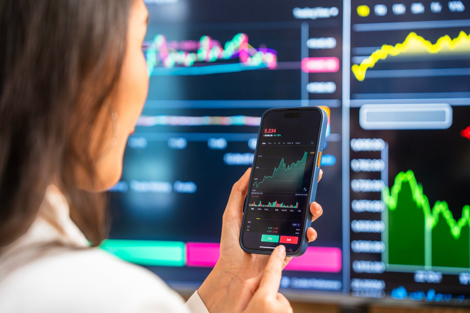 A businesswoman examines financial charts and graphs on her smartphone, utilizing modern technology for investment analysis amidst digital screens displaying stock data.
