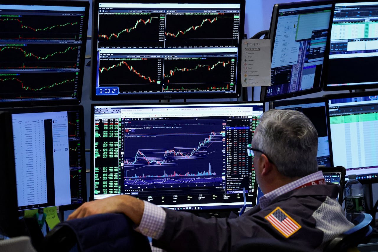 A stock trader is shown looking at several computer screens.
