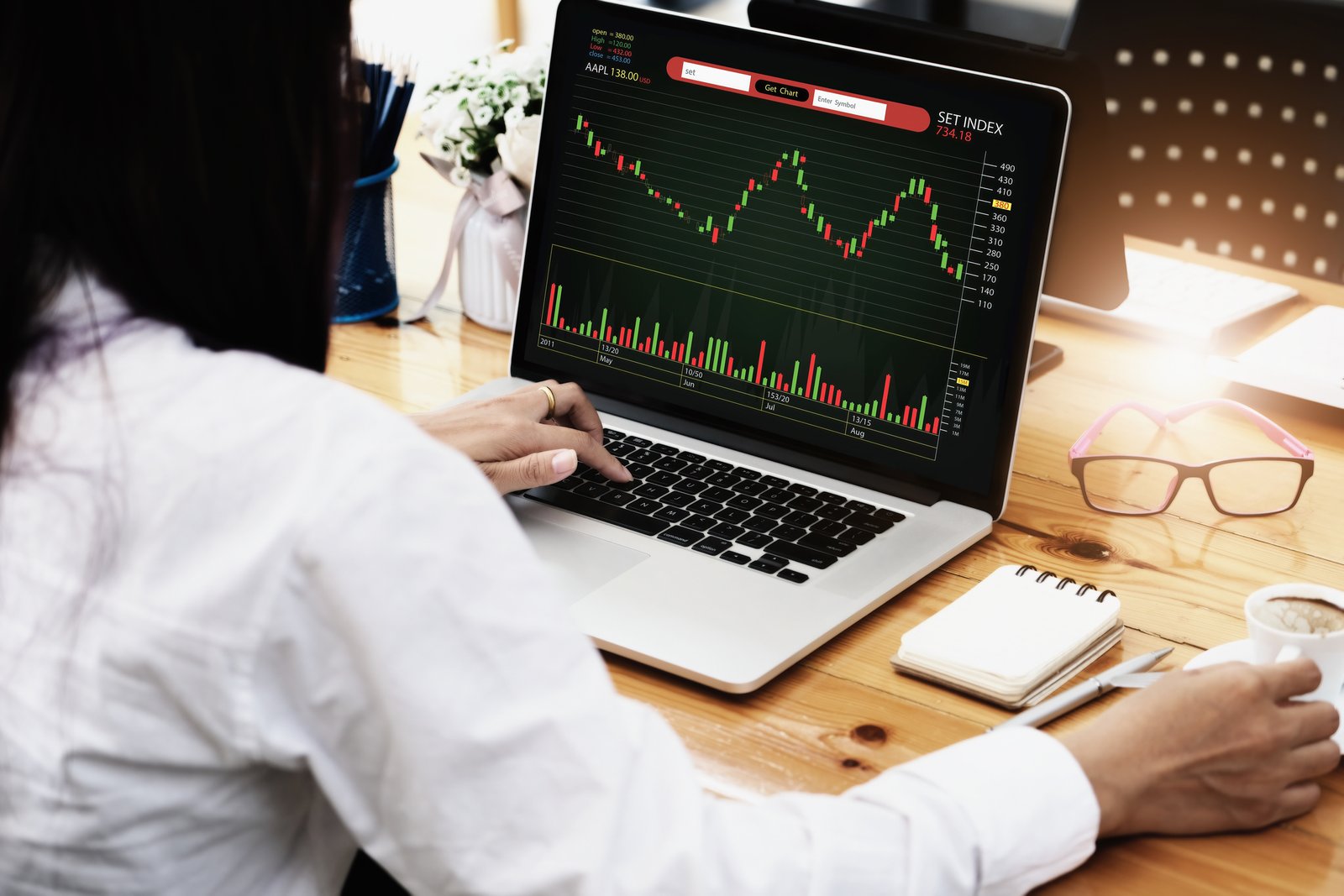 woman looking at a stock chart on her laptop while drinking coffee