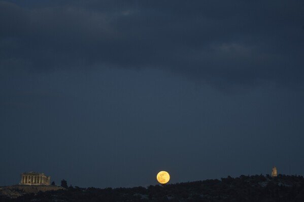 The snow moon rises behind Philopappos Hill, between the Parthenon, left, and the Philopappos Monument, right, in Athens, Greece, on Feb. 12, 2025. (AP Photo/Petros Giannakouris)