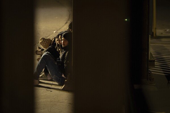 A group of migrants wait to be processed between two border walls separating Mexico and the United States after crossing illegally before dawn, Jan. 21, 2025, in San Diego. (AP Photo/Gregory Bull)