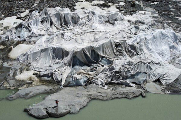 The Rhone Glacier near Goms, Switzerland, is partially covered with sheets as Matthias Huss, head of the Swiss glacier monitoring group GLAMOS, stands nearby, on June 10, 2025. (AP Photo/Matthias Schrader)