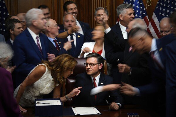 Republican members of Congress reach to shake hands with Speaker of the House Mike Johnson, R-La., center bottom, after Johnson signed President Donald Trump's bill of tax breaks and spending cuts, on July 3, 2025, at the Capitol in Washington. (AP Photo/Julia Demaree Nikhinson)
