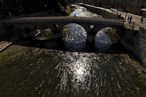 A person walks on a bridge over the Miljacka River, which is almost dried-up and covered with algae, during a heat wave and drought in Sarajevo, Bosnia-Herzegovina, on Aug. 10, 2025. (AP Photo/Armin Durgut)