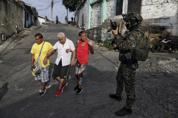 Residents walk past a soldier patrolling the Siloe neighborhood in Cali, Colombia, on Sept. 11, 2025. (AP Photo/Santiago Saldarriaga)