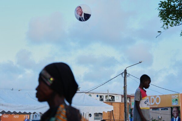 A balloon bearing the image of President Alassane Ouattara floats above supporters during a campaign rally in Koumassi, Abidjan, Ivory Coast on Oct. 22, 2025. (AP Photo/Misper Apawu)