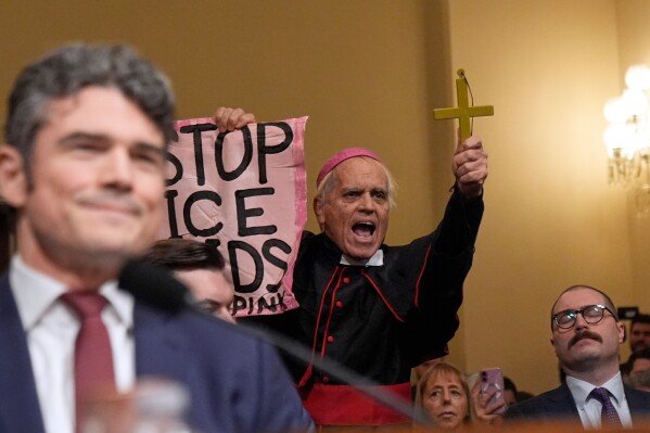 Joseph Kent, director of the National Counterterrorism Center, left, smiles as a protester interrupts during the House Committee on Homeland Security on Capitol Hill in Washington, Thursday, Dec. 11, 2025. (AP Photo/Mark Schiefelbein)