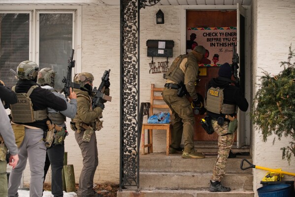 A federal immigration officer uses a battering ram to break down a door before making an arrest Sunday, Jan. 11, 2026, in Minneapolis. (AP Photo/John Locher)