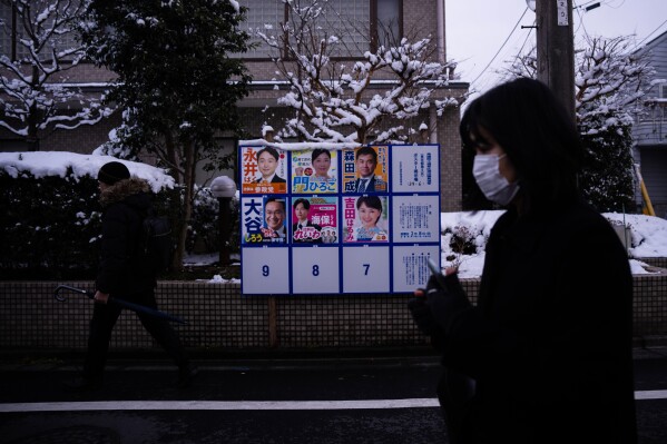 A pedestrian passes an election board displaying posters of candidate for the lower house election in Tokyo, Sunday, Feb. 8, 2026. (AP Photo/Louise Delmotte)