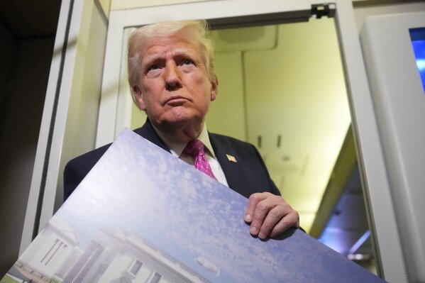 President Donald Trump holds a rendering of the proposed new East Wing of the White House as he speaks to reporters aboard Air Force One en route from West Palm Beach, Fla., to Joint Base Andrews, Md., March 29, 2026. (AP Photo/Mark Schiefelbein, File)