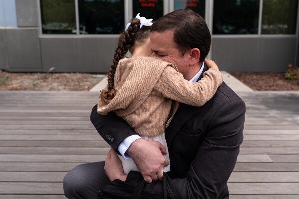 Milenko Faria, whose wife, Dr. Rubeliz Bolivar, is in immigration custody, hugs their daughter, Milena, after his asylum interview at the U.S. Citizenship and Immigration Services facility in Tustin, Calif., Thursday, April 16, 2026. (AP Photo/Jae C. Hong)