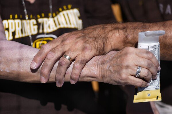 A man applies sunscreen to a woman's arm before a spring training baseball game between the San Diego Padres and the Chicago White Sox in Phoenix, Feb. 28, 2024. (AP Photo/Ashley Landis, File)