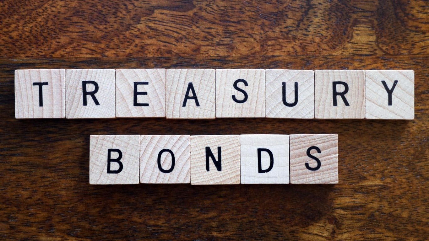Wooden letter tiles spelling 'TREASURY BONDS' arranged on a rustic dark brown wooden surface. The word 'TREASURY' is on the top row, and 'BONDS' is centered below it. The tiles are light-colored wood with black capital letters.