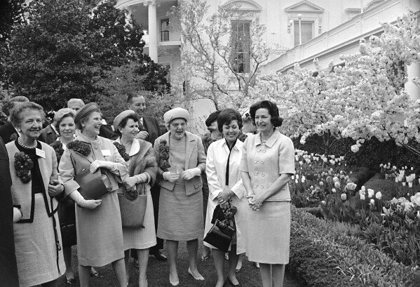 First lady Lady Bird Johnson, right, stands near tulips and a flowering crabapple tree with leaders of a 