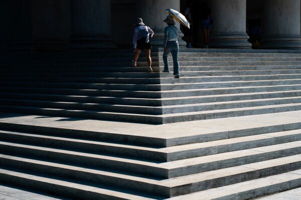Visitors walk up the front steps of the Jefferson Memorial while carrying a sun umbrella during an extreme heat advisory, Thursday, July 2, 2026, in Washington. (AP Photo/Nathan Howard)